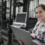 Portrait confident female technician with laptop working in server room