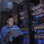 Focused male IT technician using digital tablet in dark server room