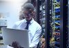 Cropped shot of a IT technician working on his laptop while standing inside of a server room