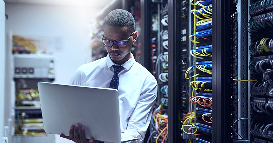 Cropped shot of a IT technician working on his laptop while standing inside of a server room