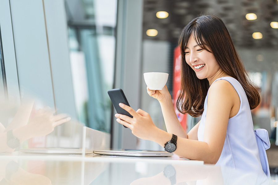 Asian woman using mobile phone and drinking a cup of coffee in modern coffee shop