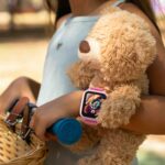 Girl riding a scooter while holding her teddy bear and wearing a smartwatch